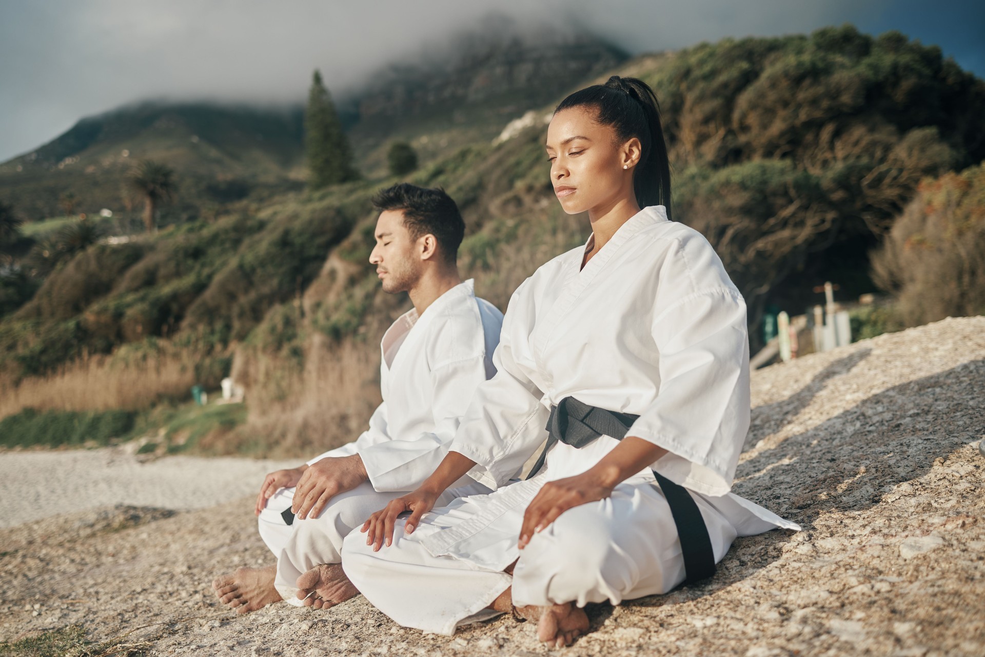 Shot of two young martial artists meditating while practicing karate on the beach