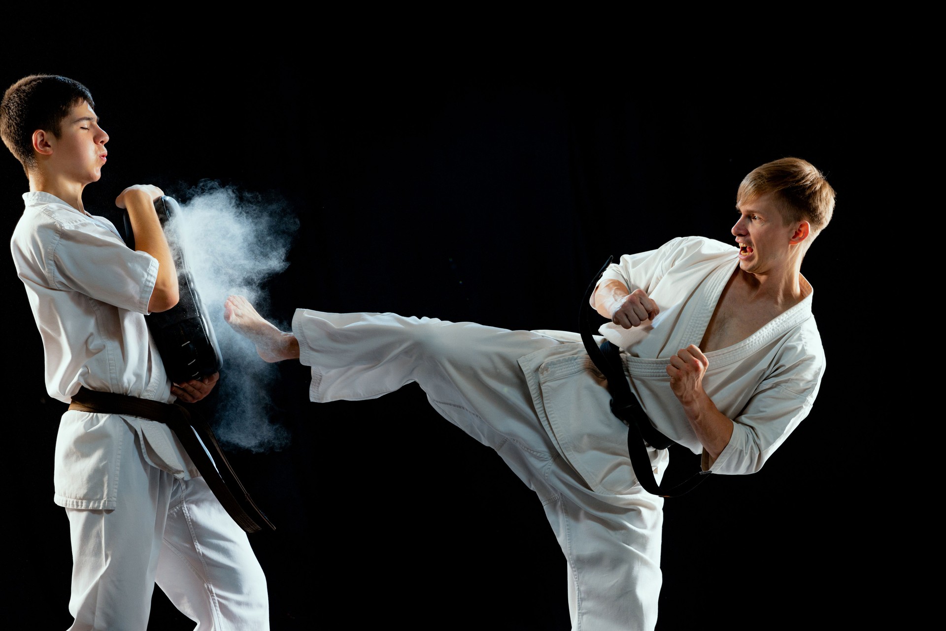 Dynamic portrait of male karate-do fighters in sports uniform training together isolated on black background. Concept of sport, education, skills, martial arts, health