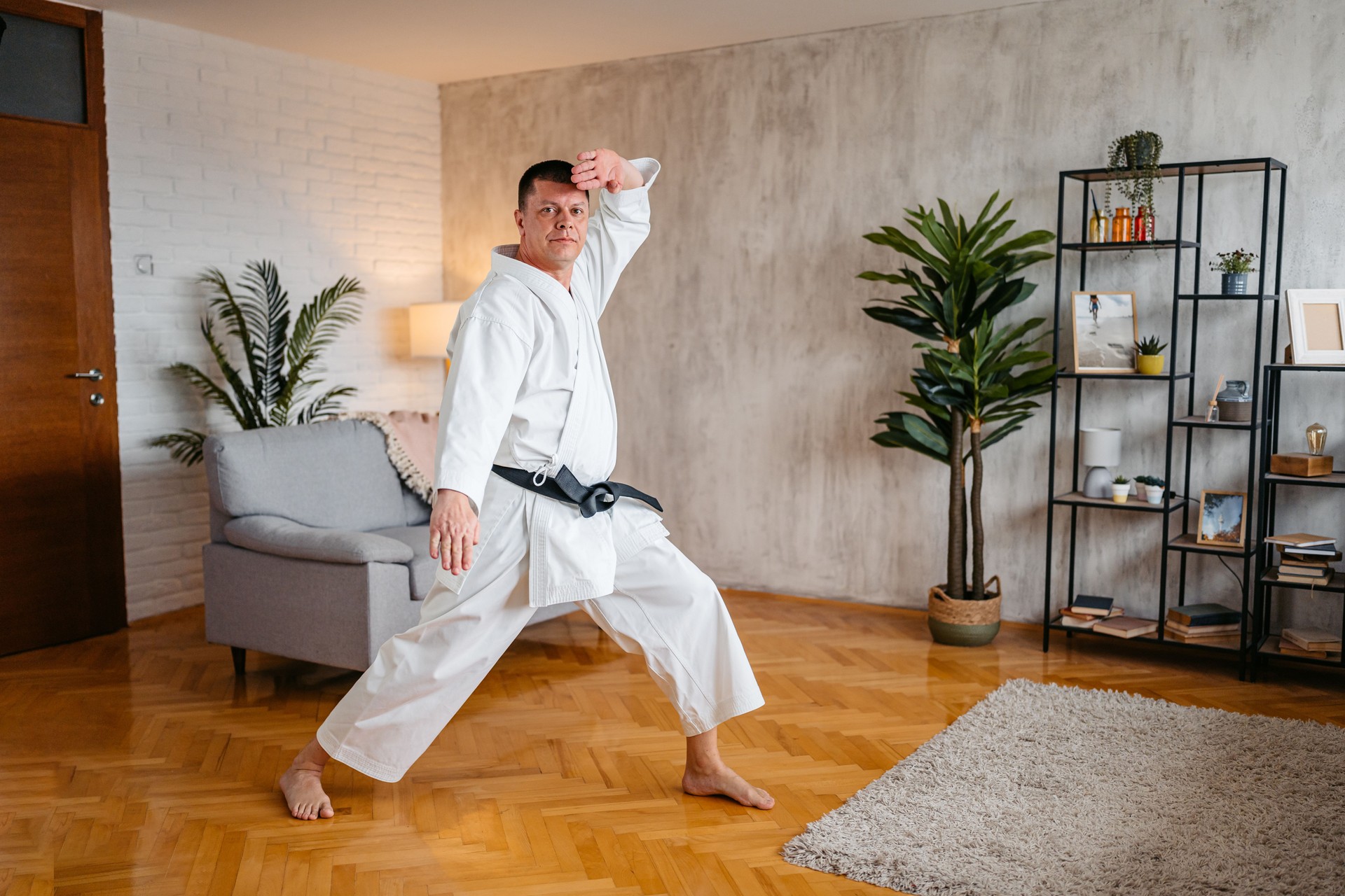 Mid-Adult Man In A White Kimono Doing Zenkutsu Dachi, Shuto Gedan Barai And Shuto Age Uke Stance In Karate At Home