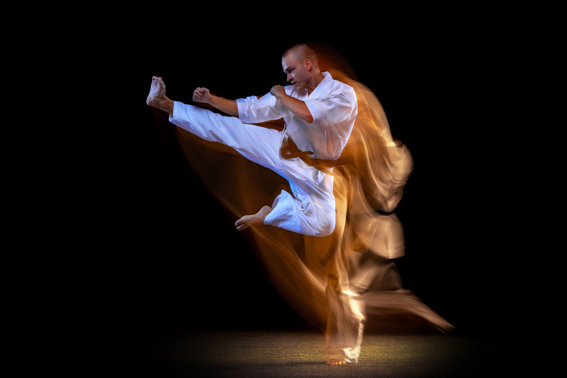 Young caucasian sportsman dressed in kimono practice in karate isolated over black background. Mixed light effect